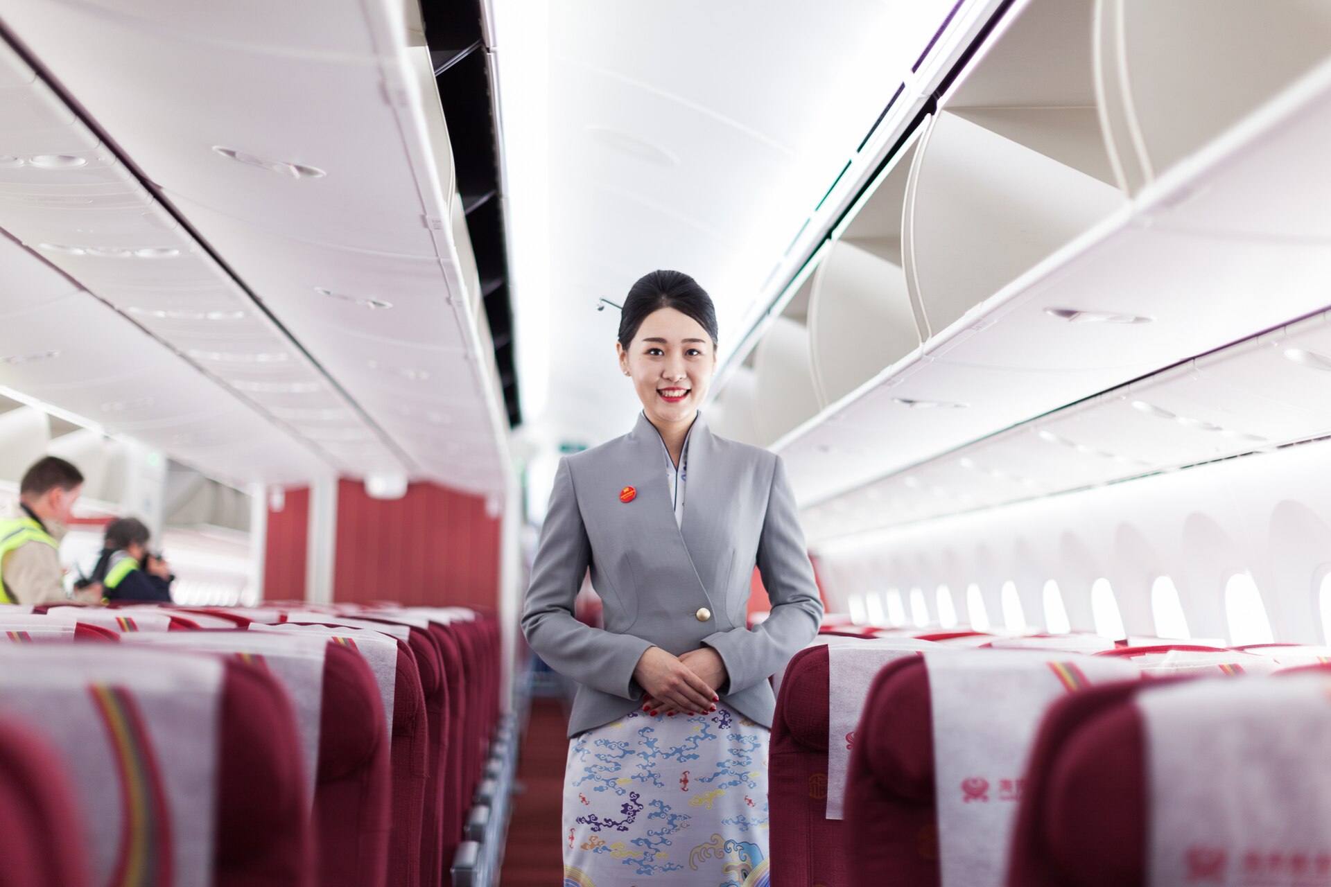 ลูกเรือ Hainan Airlines ในชุดยูนิฟอร์มสีเทา ยืนยิ้มในห้องโดยสาร