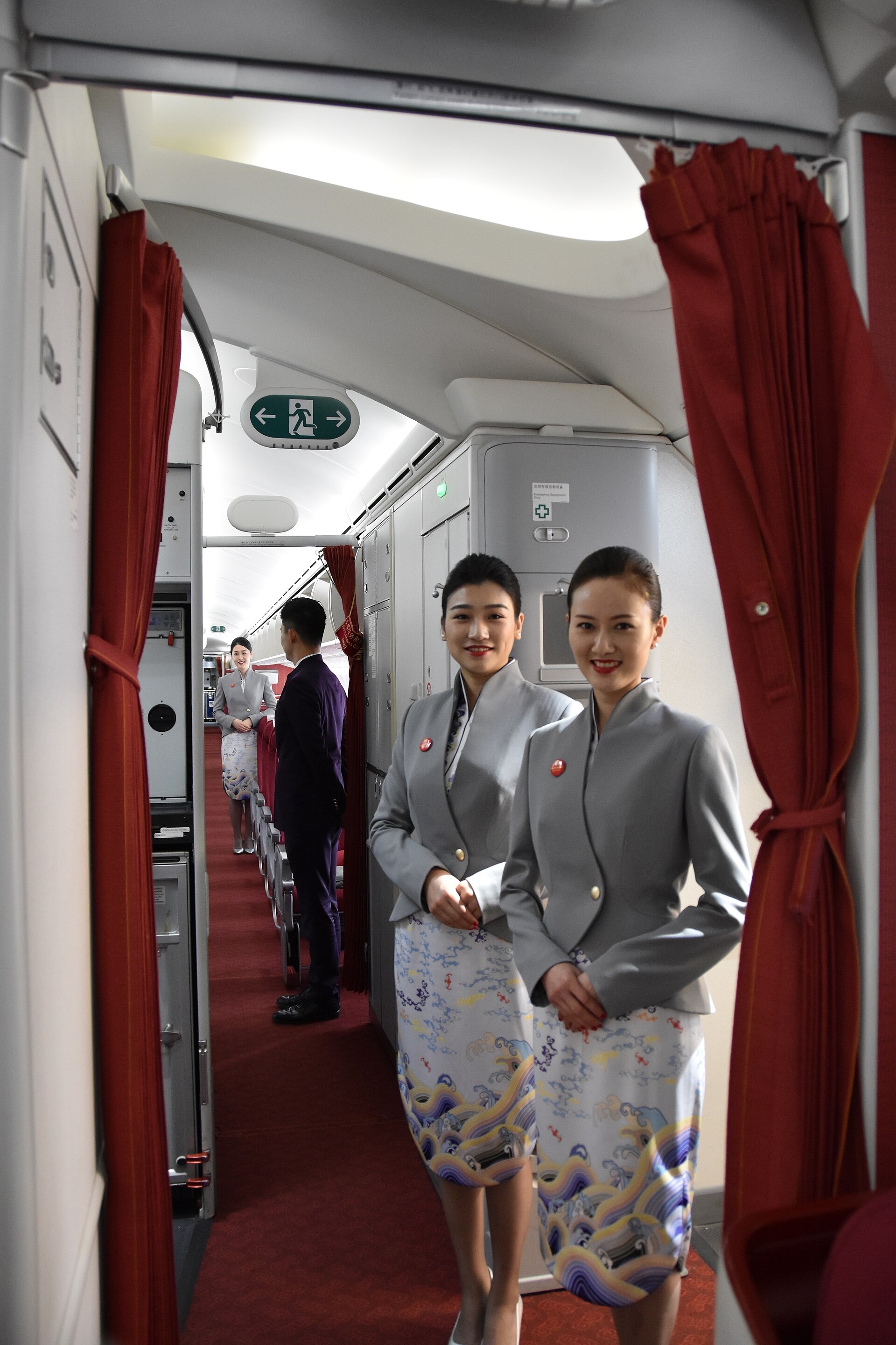 ลูกเรือ Hainan Airlines สองคนยืนยิ้มบริเวณทางเดินในห้องโดยสาร